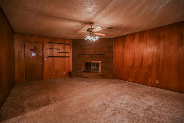 unfurnished living room featuring wood walls, carpet flooring, ceiling fan, a brick fireplace, and a textured ceiling