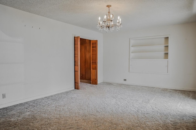 carpeted empty room featuring a notable chandelier, built in features, and a textured ceiling