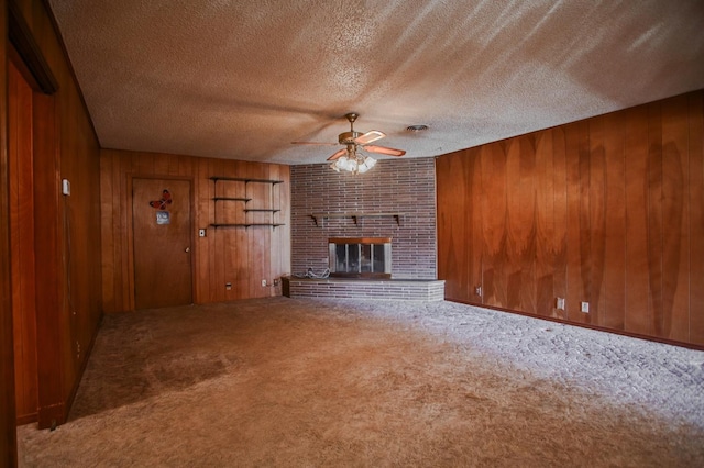 unfurnished living room with wood walls, a brick fireplace, a textured ceiling, carpet floors, and ceiling fan