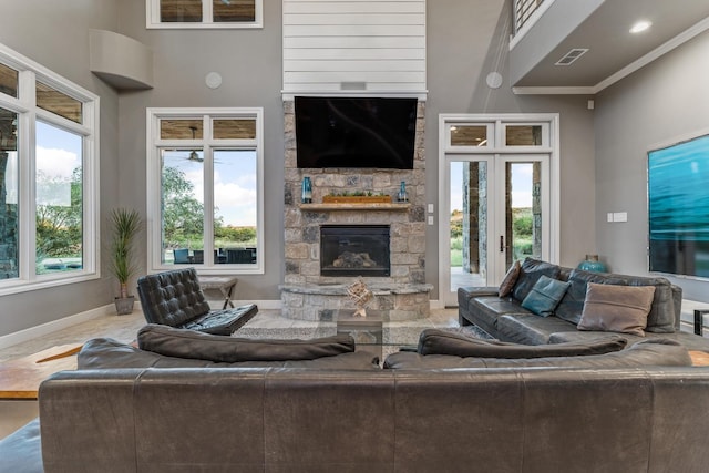 living room with a stone fireplace, ornamental molding, and a towering ceiling