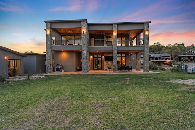 back house at dusk with a lawn, a balcony, and a patio area