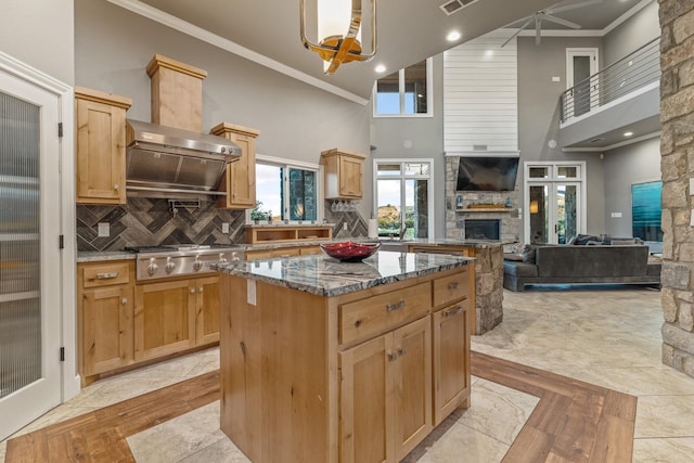 kitchen featuring dark stone countertops, a center island, ornamental molding, decorative backsplash, and a stone fireplace