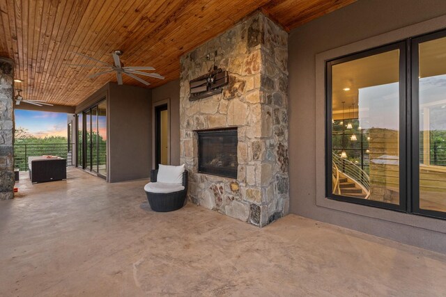 patio terrace at dusk featuring ceiling fan and an outdoor stone fireplace