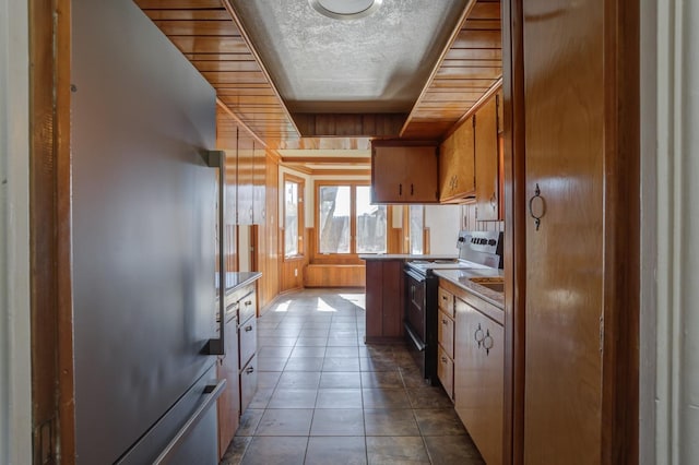 kitchen with light tile patterned floors, stainless steel refrigerator, range with electric stovetop, a textured ceiling, and wood walls