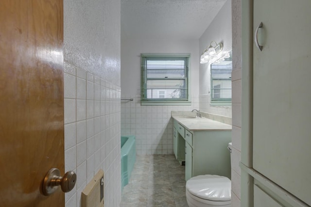 bathroom featuring a washtub, tile walls, vanity, a textured ceiling, and toilet