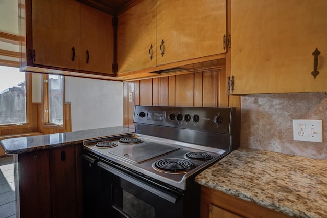 kitchen with black electric range oven, decorative backsplash, light stone counters, and kitchen peninsula