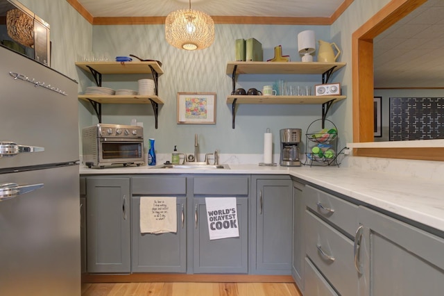 kitchen featuring sink, hanging light fixtures, stainless steel refrigerator, gray cabinets, and light stone countertops