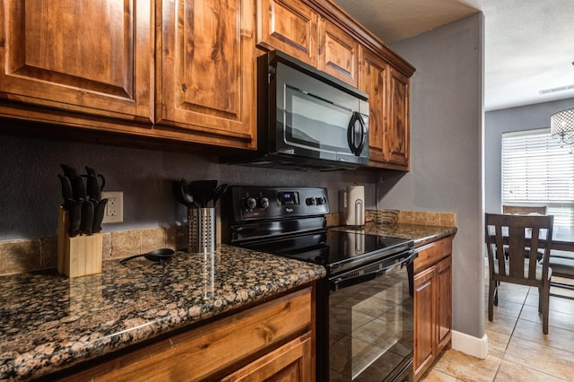 kitchen featuring dark stone countertops, light tile patterned floors, and black appliances