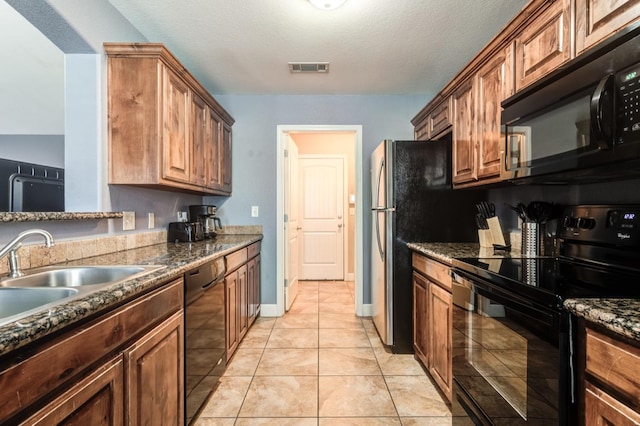 kitchen with dark stone countertops, sink, light tile patterned floors, and black appliances