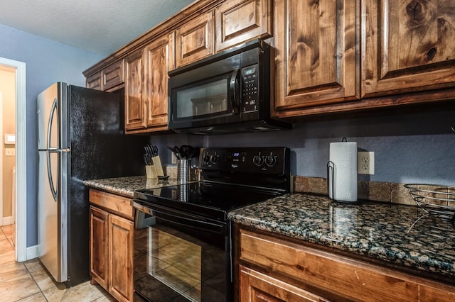 kitchen with light tile patterned flooring, a textured ceiling, dark stone counters, and black appliances