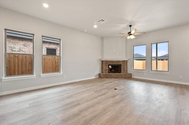 unfurnished living room with a brick fireplace, ceiling fan, and light wood-type flooring