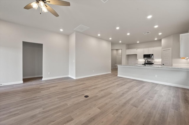 unfurnished living room with sink, light hardwood / wood-style floors, and ceiling fan