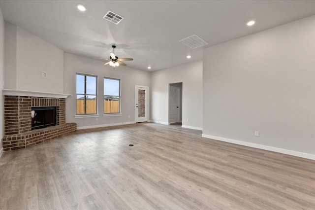 unfurnished living room featuring ceiling fan, a brick fireplace, and light wood-type flooring