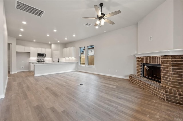 unfurnished living room featuring ceiling fan, a brick fireplace, sink, and light wood-type flooring