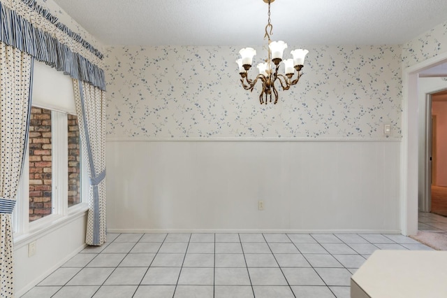 unfurnished dining area featuring an inviting chandelier, light tile patterned floors, and a textured ceiling