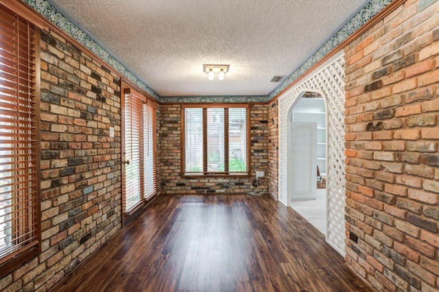 interior space with brick wall, a textured ceiling, and dark hardwood / wood-style flooring