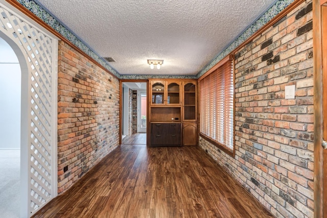 interior space featuring dark hardwood / wood-style floors, a textured ceiling, and brick wall