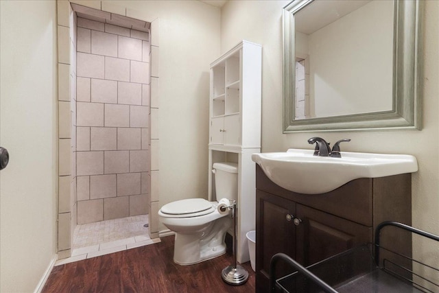 bathroom featuring a tile shower, hardwood / wood-style floors, vanity, and toilet