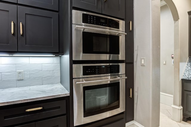 10704 Orlando Ave, Lubbock, TX 79423 - kitchen featuring dark cabinets, double oven, baseboards, light stone countertops, and decorative backsplash
