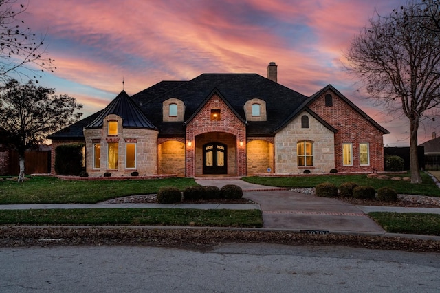 10704 Orlando Ave, Lubbock, TX 79423 - french country style house featuring french doors, stone siding, brick siding, a yard, and a chimney