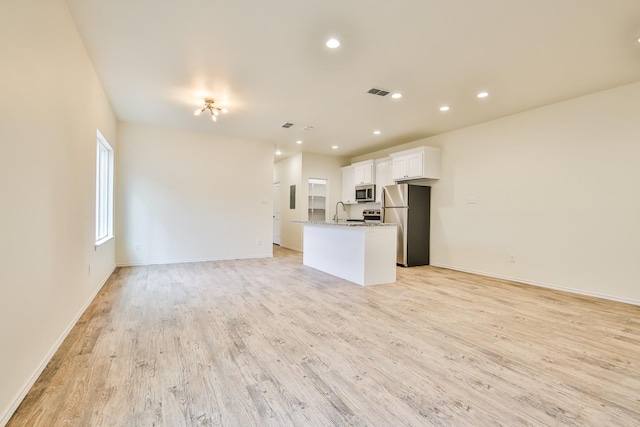 kitchen with stainless steel appliances, light stone counters, light hardwood / wood-style floors, white cabinets, and a kitchen island