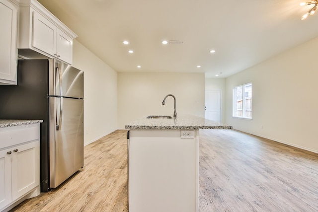 kitchen featuring stainless steel refrigerator, white cabinetry, an island with sink, sink, and light stone countertops