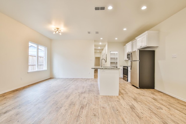 kitchen featuring white cabinetry, light hardwood / wood-style flooring, appliances with stainless steel finishes, an island with sink, and light stone countertops