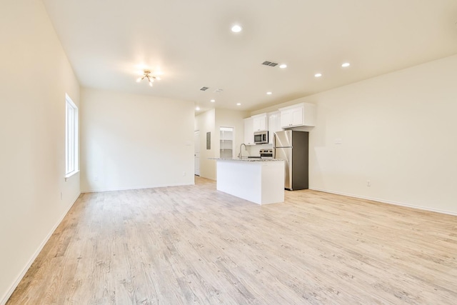 kitchen featuring appliances with stainless steel finishes, white cabinetry, an island with sink, light hardwood / wood-style floors, and light stone countertops