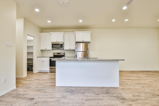 kitchen with white cabinetry, light stone counters, stainless steel appliances, and a center island with sink