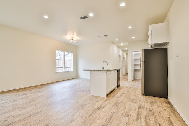 kitchen featuring an island with sink, sink, white cabinets, stainless steel dishwasher, and light stone counters