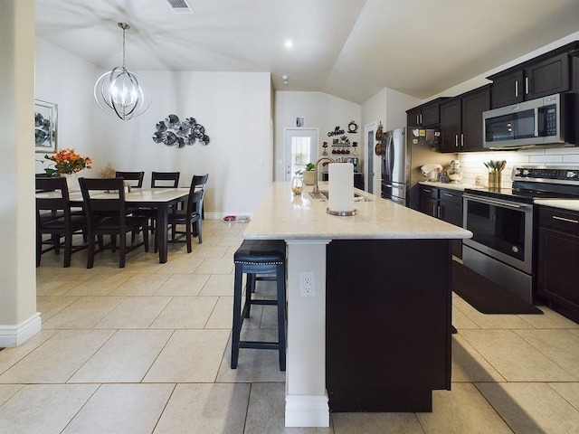 kitchen featuring pendant lighting, a breakfast bar, appliances with stainless steel finishes, a center island with sink, and vaulted ceiling