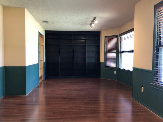 empty room featuring dark hardwood / wood-style flooring, built in shelves, and a textured ceiling