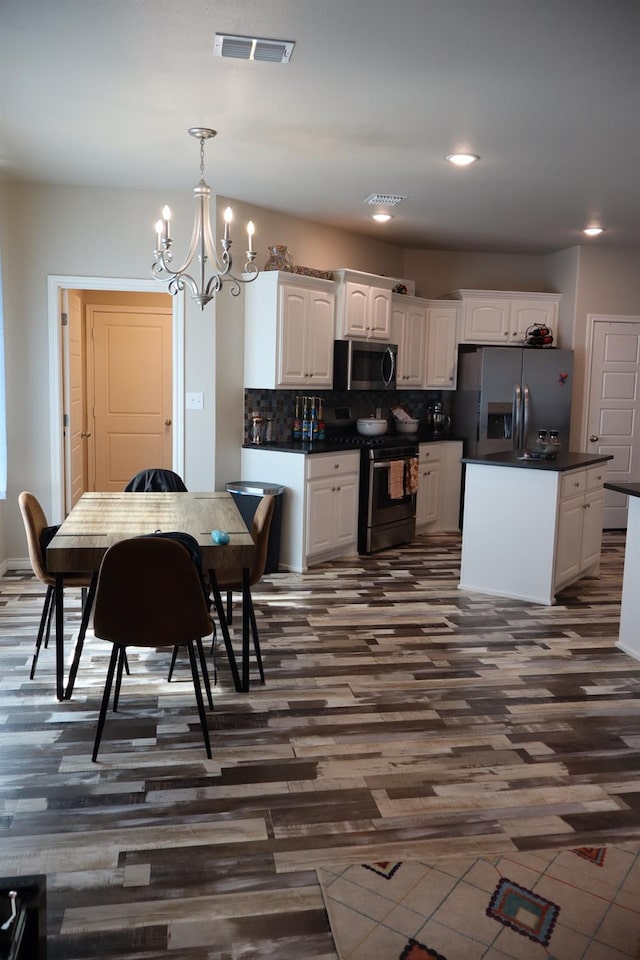 kitchen featuring stainless steel appliances, hanging light fixtures, white cabinets, and decorative backsplash