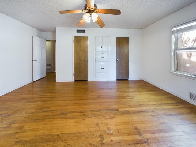 unfurnished bedroom with multiple closets, ceiling fan, a textured ceiling, and light hardwood / wood-style floors