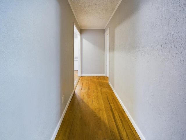 corridor featuring ornamental molding, wood-type flooring, and a textured ceiling