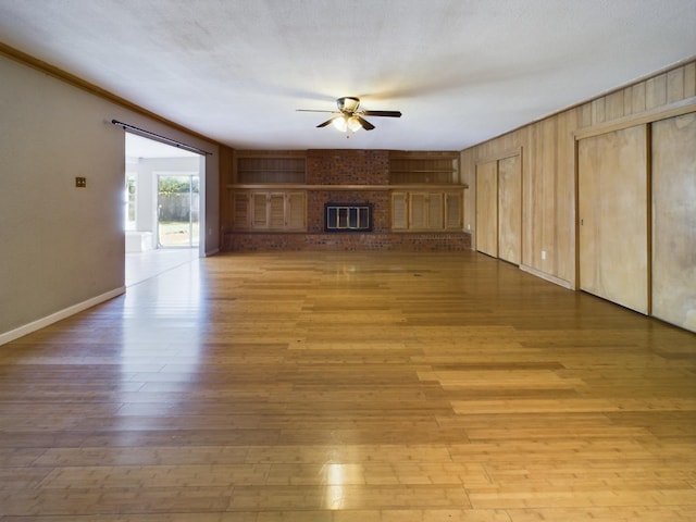 unfurnished living room featuring ceiling fan, light hardwood / wood-style floors, a brick fireplace, and a textured ceiling