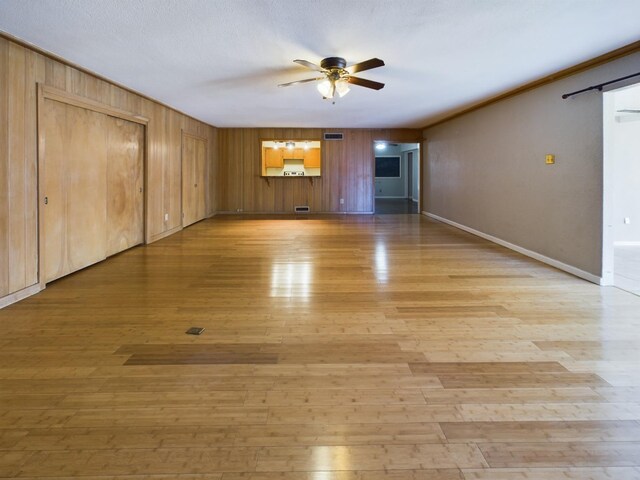 unfurnished living room featuring ceiling fan, wooden walls, a textured ceiling, and light wood-type flooring