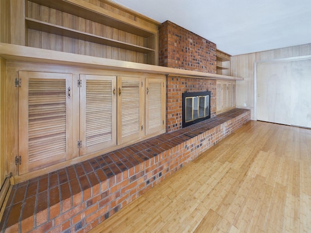 unfurnished living room featuring built in shelves, wooden walls, hardwood / wood-style floors, and a brick fireplace