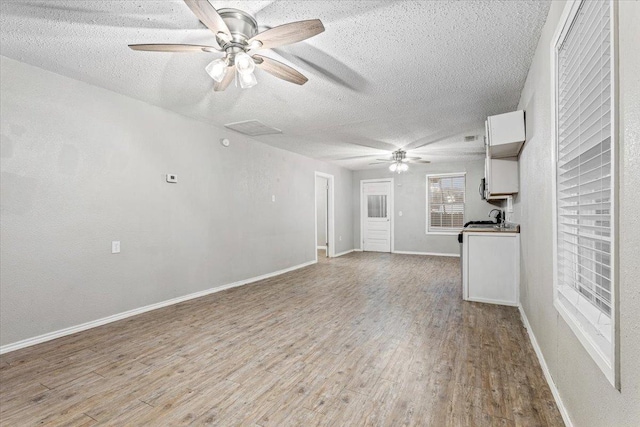 unfurnished living room with ceiling fan, light hardwood / wood-style floors, and a textured ceiling