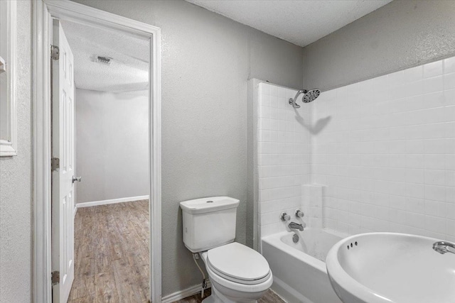 bathroom featuring tiled shower / bath, hardwood / wood-style floors, toilet, and a textured ceiling