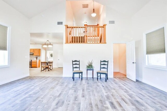 living area with light wood-type flooring, a chandelier, and high vaulted ceiling