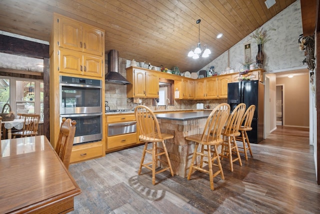 kitchen with a breakfast bar, a chandelier, light hardwood / wood-style flooring, stainless steel appliances, and wall chimney range hood