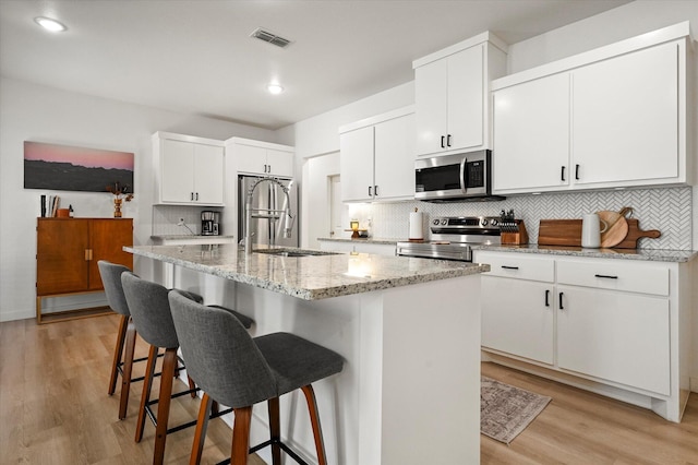 6937 12th St, Lubbock, TX 79416 - kitchen featuring a breakfast bar area, tasteful backsplash, appliances with stainless steel finishes, light wood-style flooring, and visible vents
