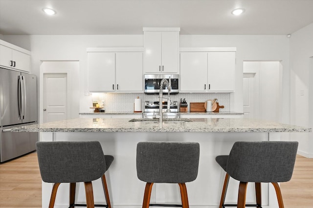 6937 12th St, Lubbock, TX 79416 - kitchen with white cabinetry, tasteful backsplash, a breakfast bar area, light wood-style flooring, and appliances with stainless steel finishes