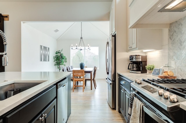 kitchen with appliances with stainless steel finishes, decorative backsplash, custom exhaust hood, hanging light fixtures, and light hardwood / wood-style floors