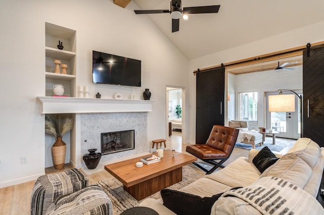 living room featuring a fireplace, a barn door, ceiling fan, and light wood-type flooring