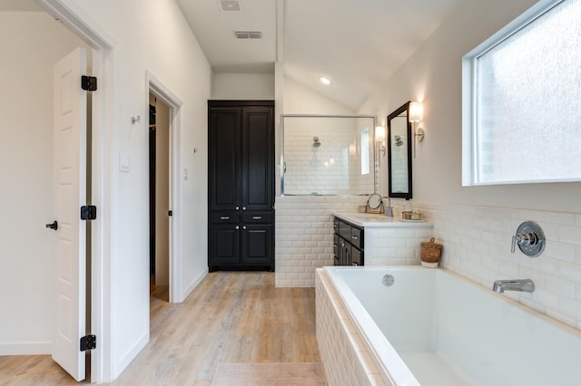 bathroom featuring a relaxing tiled tub, vanity, vaulted ceiling, and wood-type flooring