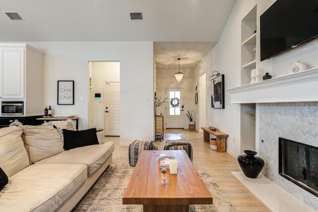 living room with built in shelves, light hardwood / wood-style floors, and a tile fireplace