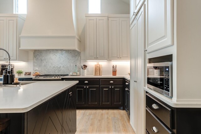 kitchen featuring sink, custom exhaust hood, light hardwood / wood-style flooring, decorative backsplash, and white cabinets