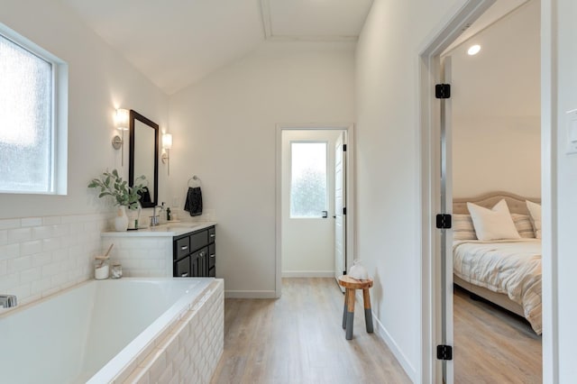 bathroom featuring lofted ceiling, vanity, wood-type flooring, and tiled tub